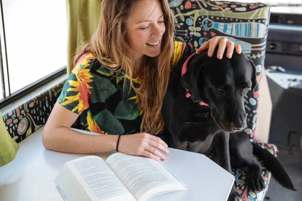 Feliz jovem mulher lendo um livro e brincando com seu cão em um c — Fotografia de Stock