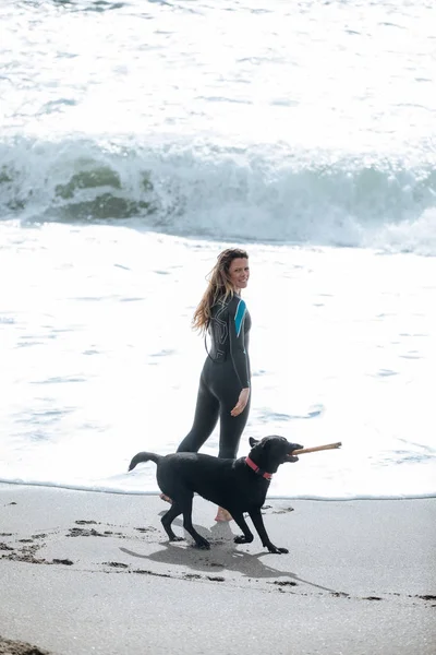 Uma jovem mulher vestindo um fato de mergulho brincando com seu cão nos mares — Fotografia de Stock