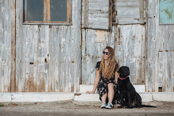 Feliz jovem mulher sentada com seu cão preto em fron de madeira velha — Fotografia de Stock