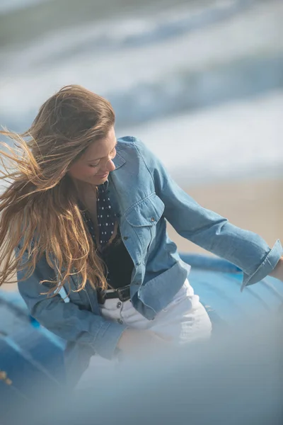 Feliz jovem sentada e posando no barco azul na frente o — Fotografia de Stock