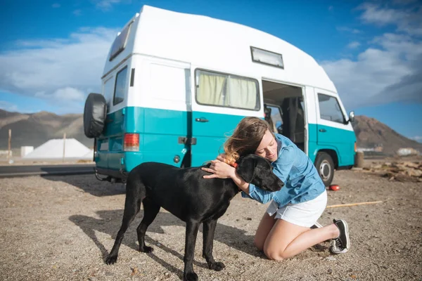 Jovem mulher abraçando seu cão na frente de um azul clássico van no th — Fotografia de Stock
