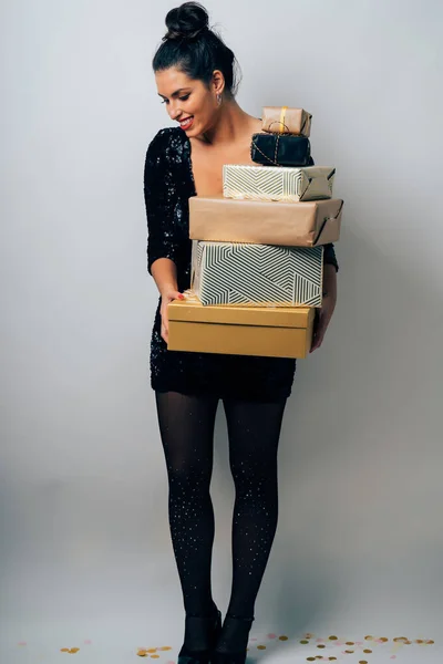 Retrato de una hermosa y feliz mujer vestida para la fiesta cerrar un montón de regalos de Navidad y confeti sobre fondo blanco . — Foto de Stock