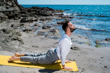 Adam sahilde meditasyon yapıyor ve pratik yapıyor.