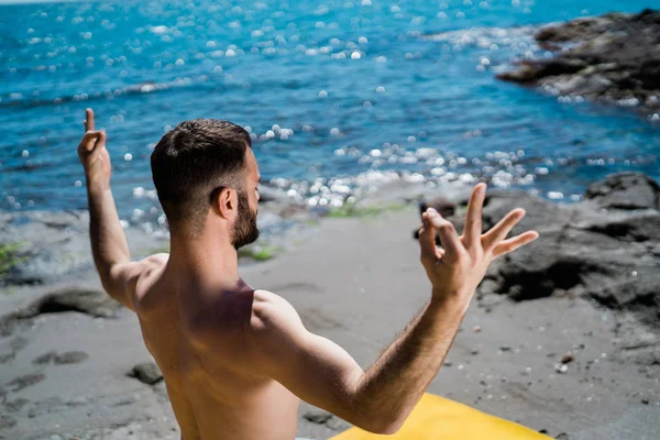 Ajuste o homem jovem que medita em uma posição do Yoga em uma praia — Fotografia de Stock