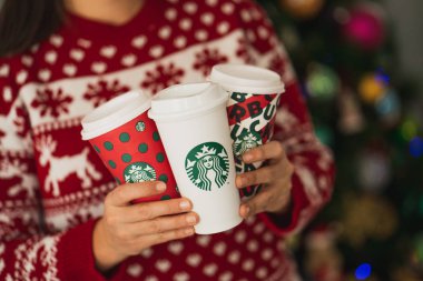 New York, Usa - 4 Aralık 2019: Üç Uzun Starbucks Kupası 'nda Noel süveteri giyen bir kadının yakın çekimi. 2019 Noel Tatili için Bir Orijinal Kupa ve İki Tasarım.