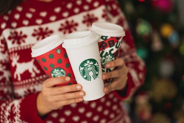 New York, Usa - 4 Aralık 2019: Üç Uzun Starbucks Kupası 'nda Noel süveteri giyen bir kadının yakın çekimi. 2019 Noel Tatili için Bir Orijinal Kupa ve İki Tasarım.
