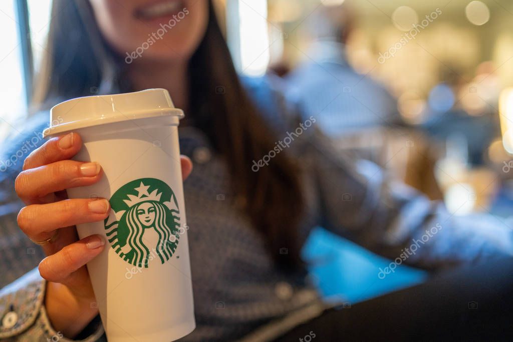 New York, USA - December 1, 2019 : Happy Caucasian Girl Holding a Tall Cup of Starbucks Coffee in Starbucks Coffee Store.