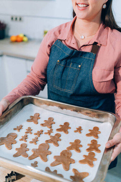 Молодая женщина печет пряничное печенье. Подготовка к Рождеству, украшенные пряники, сырое тесто, металлический резак. Имбирь ручной работы
