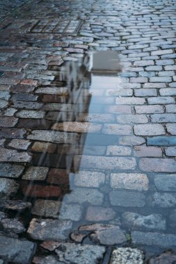 Evlerin ve gökyüzünün yansıdığı bir yolun tuğla zemininde su birikintisi.