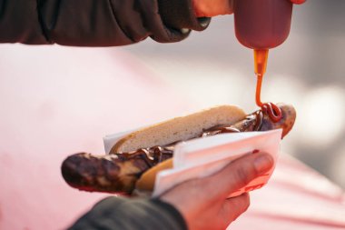 Alman pazarında ızgara domuz sosisine domates sosu, mayonez ve hardal döken bir kadın..