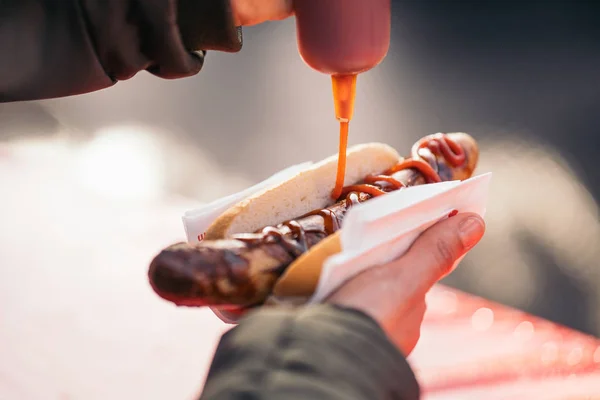 Mulher derramando molho de tomate, maionese e mostarda em uma salsicha de porco grelhada Bratwurst em um mercado alemão . — Fotografia de Stock