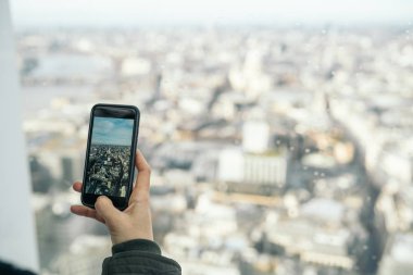 Londra 'nın finans bölgesinin panoramik bir bakış açısıyla akıllı telefonuyla dikey bir fotoğraf çeken bir kadın Gökyüzü Bahçesi' nin bakış açısından.