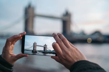 Güneşli bir kış günü Londra, İngiltere 'de Tower Bridge' de akıllı bir telefonla fotoğraf çeken bir kadın..