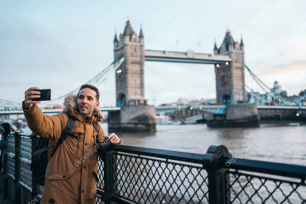 Young Man taking a photo with the smart phone to the Tower Bridge in London on a sunny winter day, London, Great Britain.