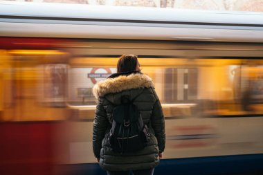 Metroda bekleyen yeşil ceketli ve sırt çantalı genç bir kadının portresi..