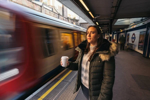 Portrait of young woman wearing green jacket with hot coffee waiting the train in metro.