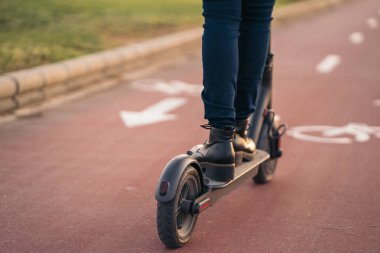 Bisiklet yolunda scooter süren genç bir kadının yakın görüntüsü.