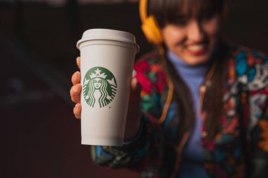 New York, Usa - 10 Ocak 2020: Bulanık gülümseyen kadın sarı kulaklıklarla müzik dinliyor ve elinde Starbucks kahvesi tutuyor.