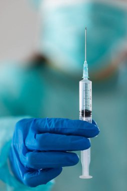 Korunaklı maskeli, kepli ve eldivenli bir kadın doktoru aşı ve şırınga kullanarak koronavirüse karşı kapatın. Korona virüsü enfeksiyonunu önlemek, aşılamak ve tedavi etmek için kullanılır.