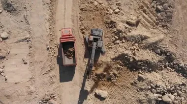 İnşaat kazıcısı endüstriyel taş ocağında çalışıyor. Kovalı bir makine kariyerinde kamyonu yükler..