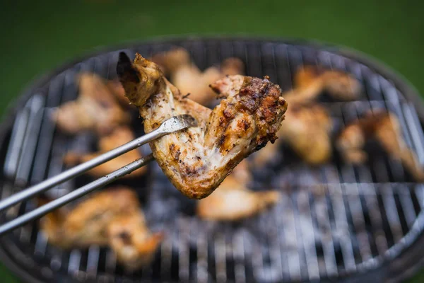 夏の週末に焼く 焼きたての肉 鶏の羽をトングのペアで持ち上げる うまい焼き肉の盛り合わせ — ストック写真