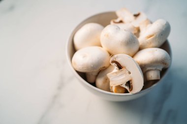 Beyaz taş arka planda izole edilmiş bir kasede taze ve dilimlenmiş şampiyon mantarları.