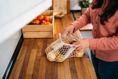 Kadın tekrar kullanılabilir organik pamuk ağların içinde sebze alışverişini ahşap arka planda tutuyor. Sıfır atık, plastiksiz konsept. Sürdürülebilir yaşam tarzı.