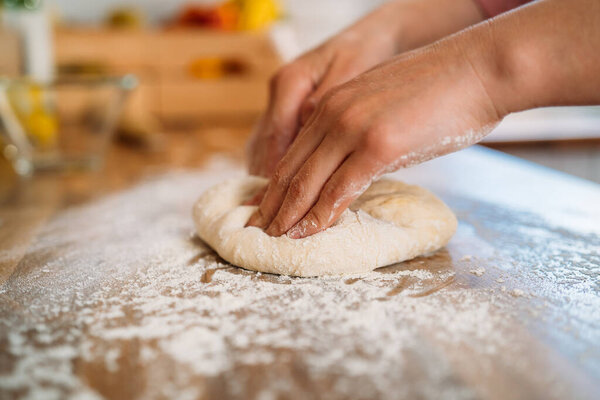 Woman kneading the dough to make a pizza in her home kitchen