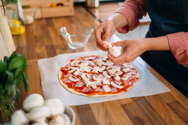Geleneksel margarita pizzasına mozzarella peyniri ekleyen kadın elleri. Orijinal İtalyan pizzasının hazırlığı