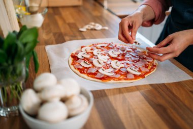 Yemek konsepti. Taze çiğ İtalyan pizzası, geleneksel stil hazırlığı. Pizzanın kadınsı elleri pizzaya mantar ekler, gerçek bir iç mekanda pizza pişirir, ahenkli bir yaşam tarzı yaratır..