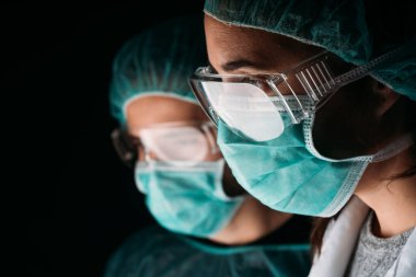 Tıbbi maske, gözlük, tıbbi kapsül ve virüs koruyucu giysiler takan iki kadın ve erkek doktor fotokopi odası olan siyah arka planda çalışıyor. COVID-19 Koronavirüs salgını.