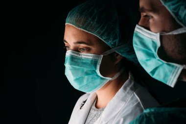Tıbbi maske, tıbbi kapsül ve virüs koruyucu giysiler giyip siyah arka planda fotokopi çeken iki kadın ve erkek doktor. COVID-19 Koronavirüs salgını.