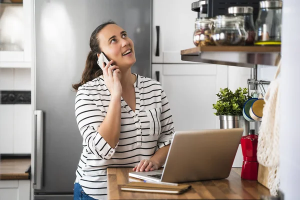 Mujer Joven Feliz Hablando Teléfono Inteligente Utilizando Ordenador Portátil Cocina — Foto de Stock