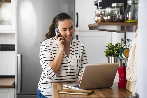 Mujer Joven Feliz Hablando Teléfono Inteligente Utilizando Ordenador Portátil Cocina — Foto de Stock
