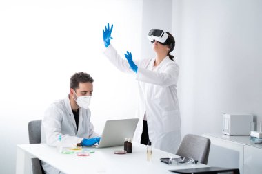 Modern biyoloji laboratuvarında çalışan genç bilim adamları veya araştırmacılar. Petri kabında numunelerle çalışan bir adam ve araştırmayı görselleştirmek için sanal gerçeklik gözlüğü takan bir kadın. Biyokimya ve teknoloji kavramı.