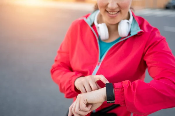 Close up of a Young woman runner wearing headphones looking at her sport watch and checking progress on smart watch. Sport, active life.