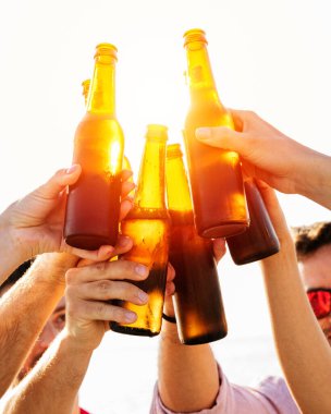 Şerefe! Bir grup mutlu insan yaz günbatımında bira şişeleriyle kadeh kaldırıyor. Kutlama konsepti