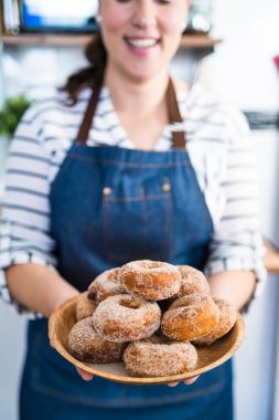 Kot önlüklü genç bir kadının elinde bir tabak taze pişmiş ev yapımı şekerli çörekleri satılığa hazır halde tutarken.