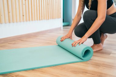 Evde çalıştıktan sonra turkuaz yoga ya da spor paspası katlayan güzel bir genç kadın. Sağlıklı yaşam, sağlıklı kavramları koru..