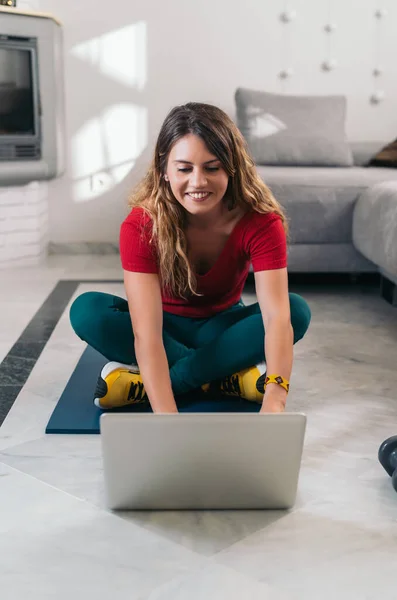 Mujer haciendo deportes en una estera siguiendo clases en línea con el ordenador portátil en casa — Foto de Stock