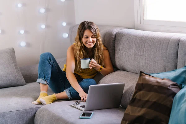 Mujer sentada en el sofá usando el ordenador portátil y tomando café — Foto de Stock