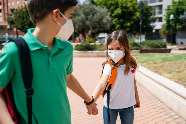 Jongen en meisje met rugzakken en maskers gaan naar school in coronavirus pandemie — Stockfoto