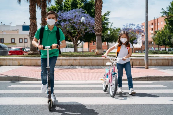 Ragazzo e ragazza che indossano maschere e cavalcando uno scooter e una bicicletta per strada — Foto Stock