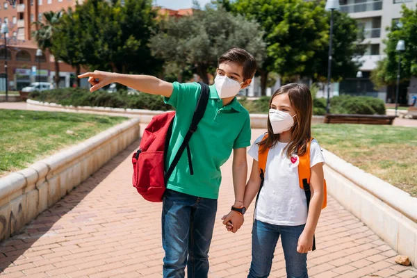 Niño y niña con mochilas y máscaras yendo a la escuela en pandemia de coronavirus —  Fotos de Stock