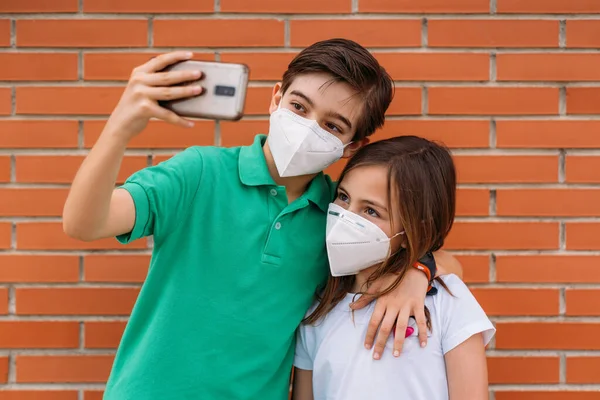 Feliz niño y niña usando máscara y tomando una selfie con el teléfono inteligente —  Fotos de Stock