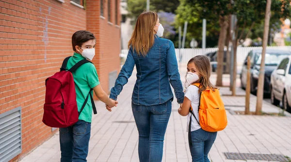 Madre con sus hijos van a la escuela con máscaras en la pandemia de coronavirus —  Fotos de Stock