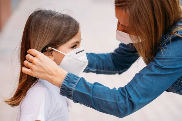 Moeder zet gezichtsmasker op haar dochtertje op straat — Stockfoto