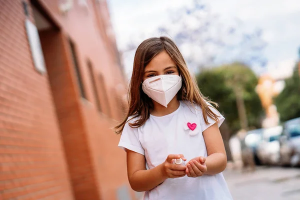 Bambina mascherata che si disinfetta le mani con gel idroalcolico . — Foto Stock