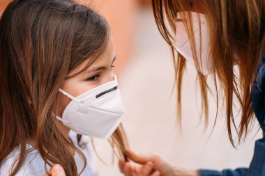 Anne sokakta kızının yüzüne maske takıyor.