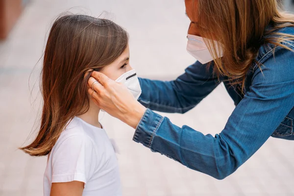 Moeder zet gezichtsmasker op haar dochtertje op straat — Stockfoto